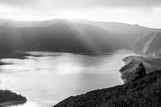 A stunning black and white photo capturing sunbeams over a tranquil mountain lake landscape.